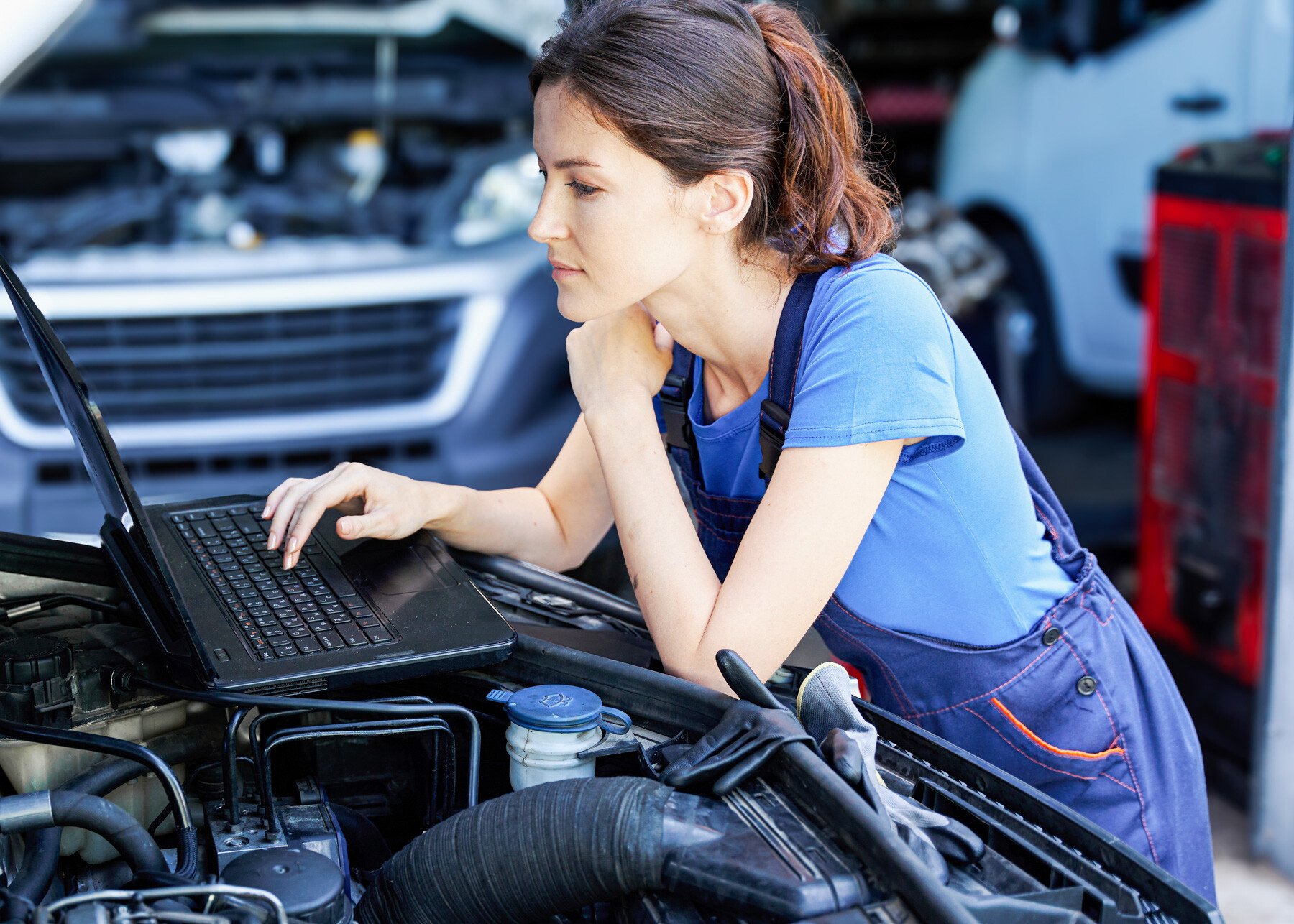 Technikerin mit Laptop an der geöffneten Motorhaube. KFZ-Technikerin prüft ihre Goya Kundenportal mit einem Laptop.